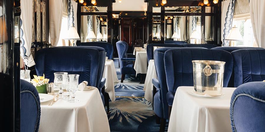 The restaurant car of the Venice Simplon-Orient-Express is decorated with rich blue velvet chairs and neatly presented tables.