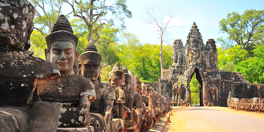 The stone gate of Angkor Thom, large stone statues line the path up to the gate.