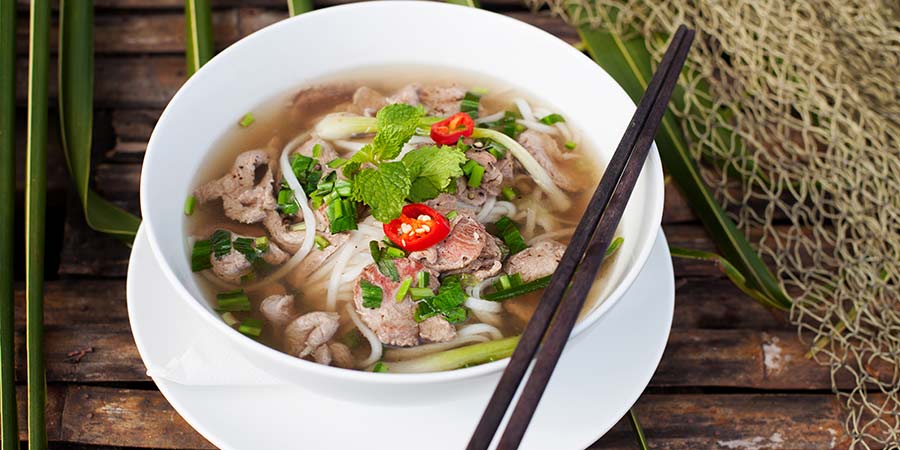 A bowl of Pho: a traditional Vietnamese soup dish, served with thick noodles, beef, coriander and red peppers.