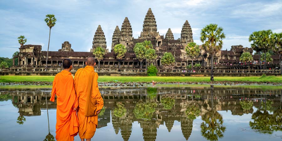 Two monks stand in front of Angkor Wat dressed in bright orange robes.